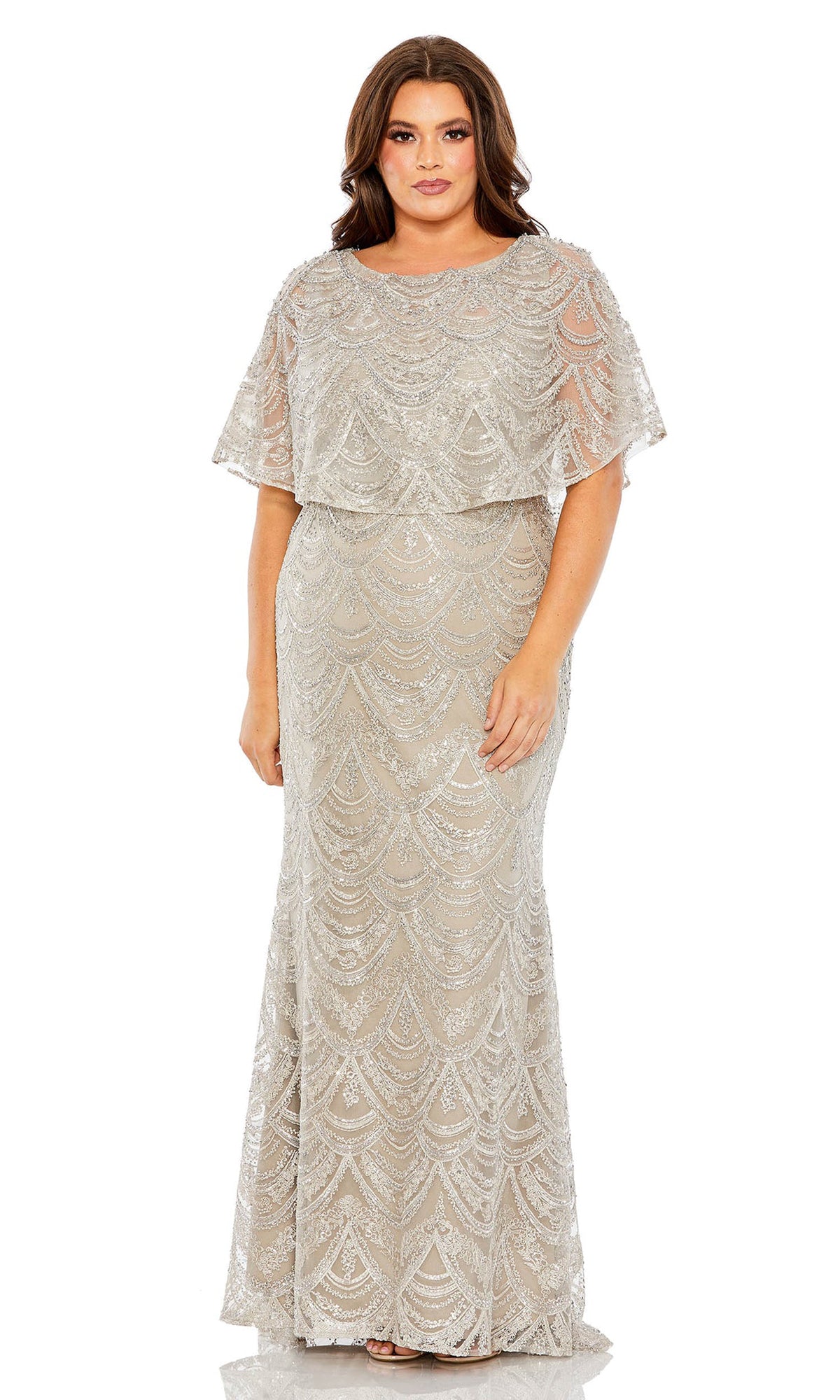 A woman wears the Long Plus-Size Formal Dress 20470 by Mac Duggal—a floor-length, silver gown with sequin embellishments, short sleeves, and a scalloped pattern.